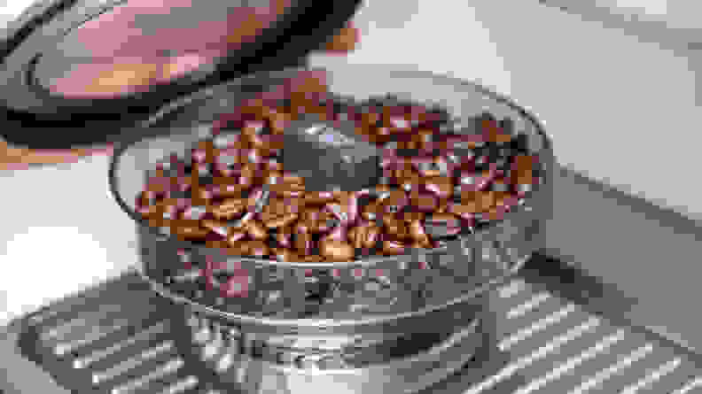 A close-up of the Barista Touch's built-in burr grinder filled with coffee beans.