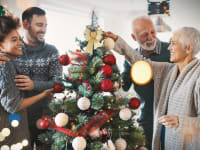 Four people decorate a Christmas tree with ornaments.