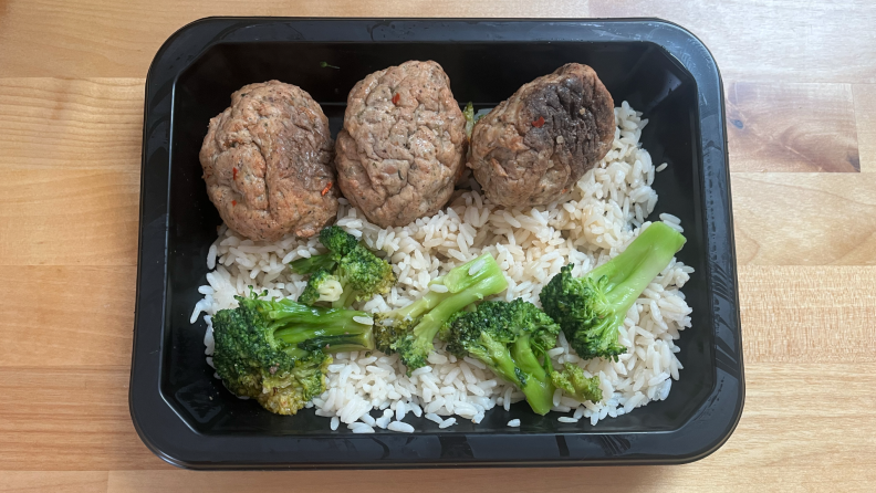 Meat, rice and broccoli inside of black plastic container.