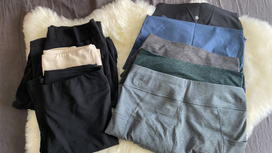 A photograph of eight pairs of solid-colored leggings in different colorways laying on top of a white sheepskin rug.