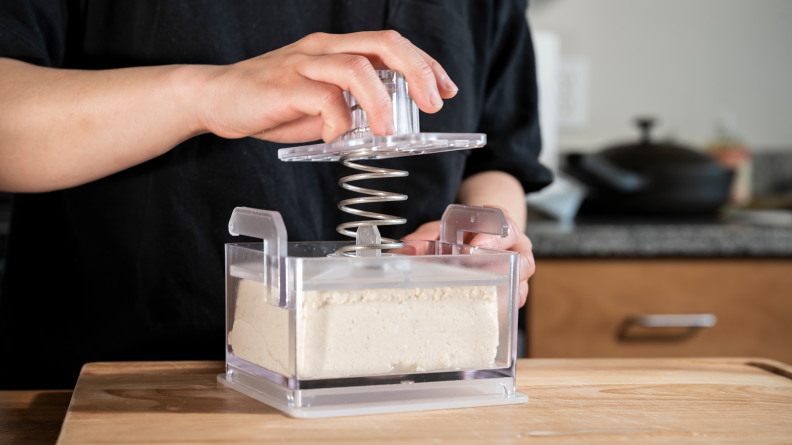 A person pressing a block of tofu with the TofuXpress