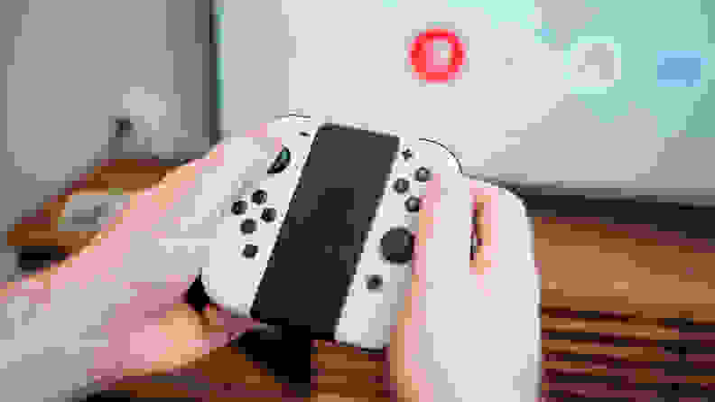 A hand holding a small nintendo switch oled joy-con controller