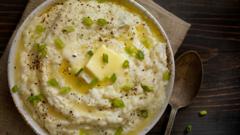 Bowl of mashed potatoes topped with butter, pepper, and scallions