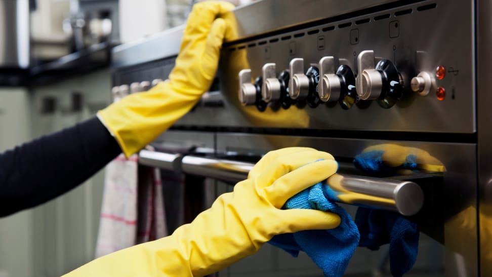 A person wipes a stainless steel oven with a microfiber towel.