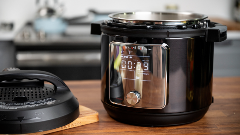 An Instant Pot Pro with the lid off on a kitchen counter. A stove is in the background with a blue pan on it.