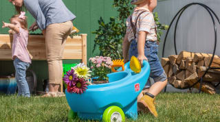 A child pulls a toy wheelbarrow full of plants