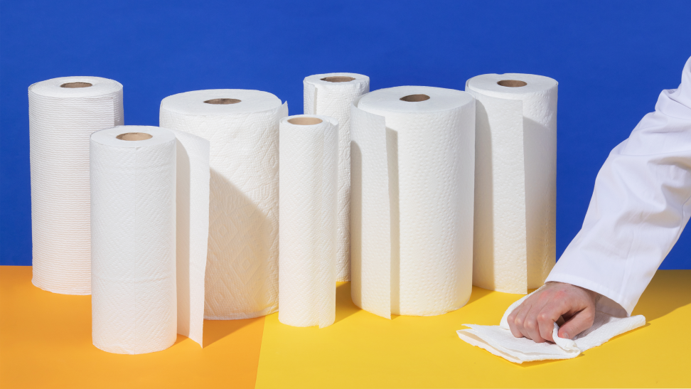 A collection of paper towels on a yellow table with a person's hand wiping the surface.