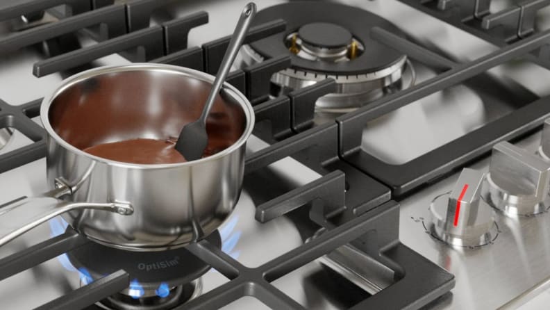 Small stainless steel pot cooking melted chocolate on stovetop.