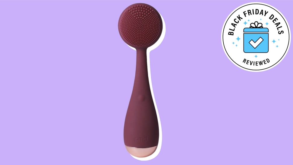 PMD Beauty facial cleansing brush against a purple background.