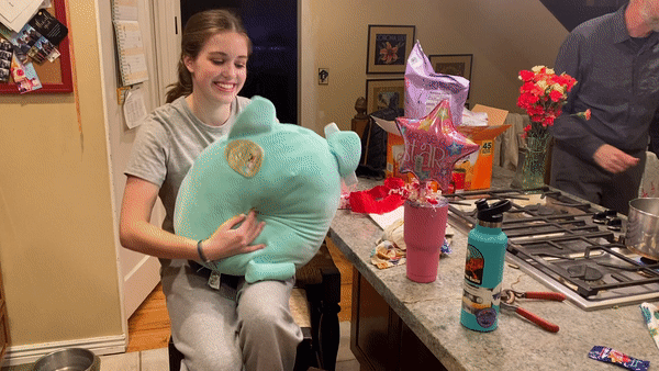 a teenage girl holds and hugs a teal green cat squishmallow