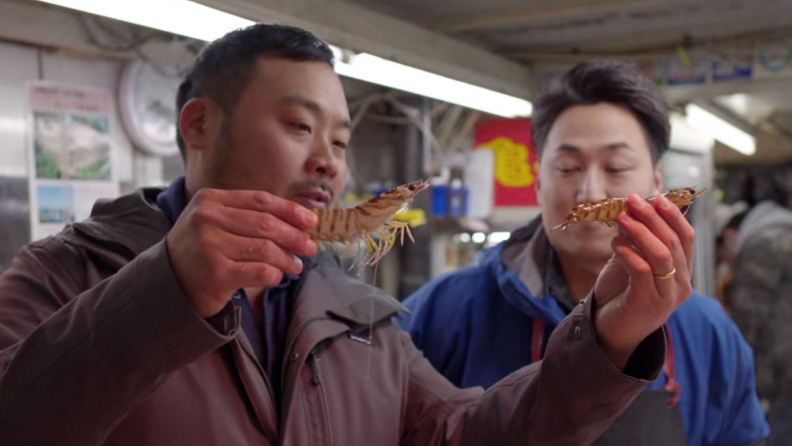 A still from Ugly Delicious featuring David Chang holding two shrimp in a marketplace.