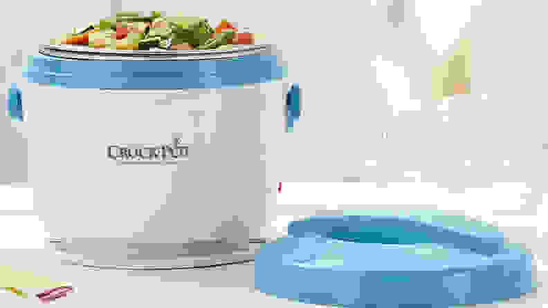 An personal-size Crock-Pot sits open on a table, with its lid beside it. It is full of a vegetable soup.