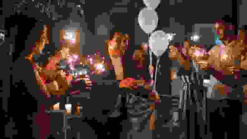 A newly married couple exits a dinner table flanked by wedding guests holding sparklers