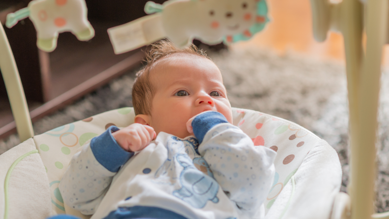 Small baby reclining in swing with hand in mouth.