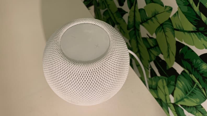 An Apple HomePod Mini smart speaker sits on a white shelf