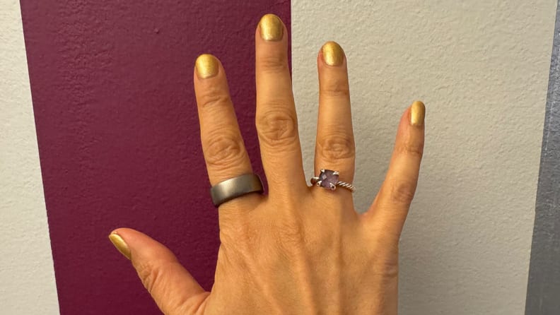 Amazfit Helio ring and a wedding ring on fingers of a hand on a colorful striped background