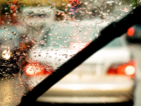 Close-up of a windshield wiper blade clearing away the rain from one side, a painterly cityscape visible beyond the windshield.