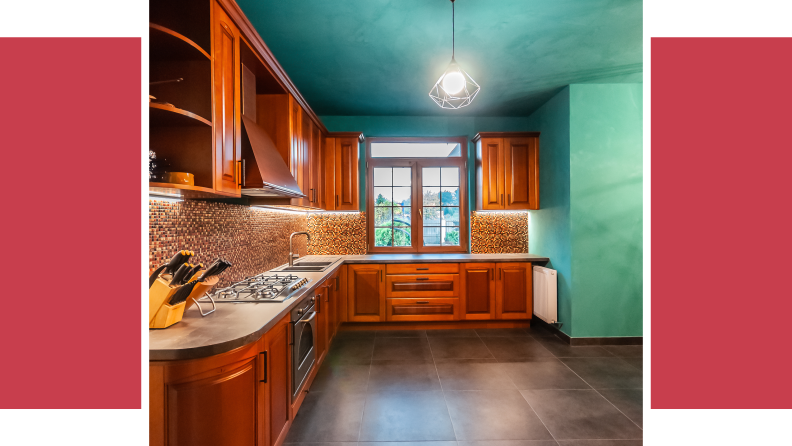 A kitchen with wooden cupboards and marble tops with freshly-painted walls and ceiling in turquoise.