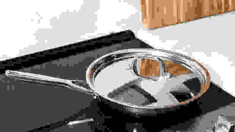 The Anolon Tri-Ply Clad Frying Pan with lid sits on a stove.