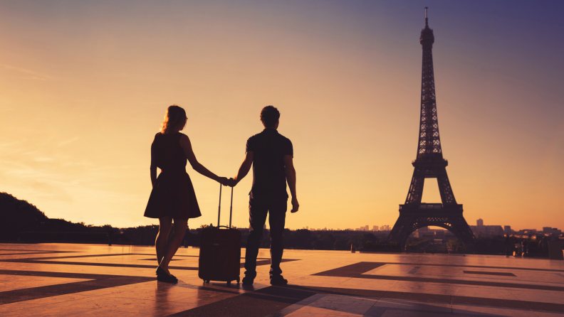 A couple strolls with a roller suitcase in Paris.