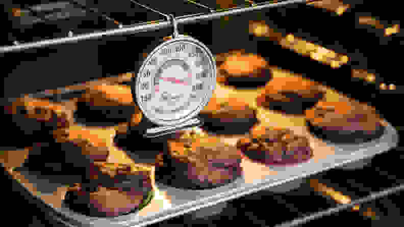 An oven thermometer hanging in front of a tray of muffins.