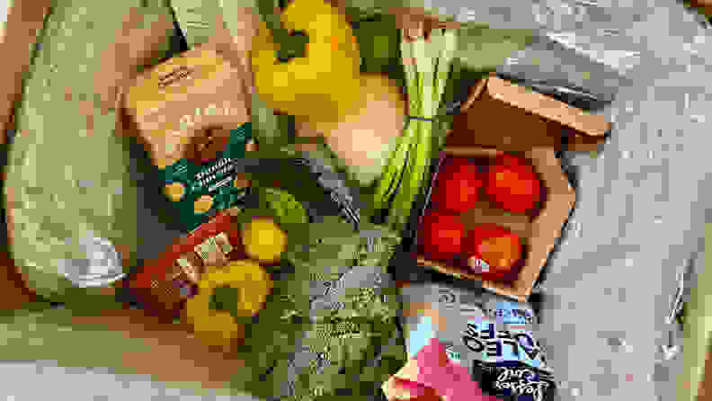 Looking into a Misfits Market box, there's fresh broccoli, yellow bell peppers, tomatoes, scallions, blueberries, chocolate chip cookies, and paleo chips.