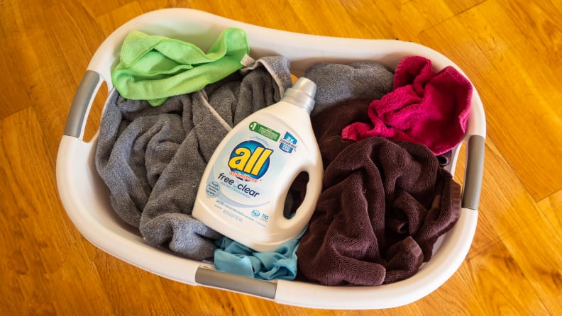 A bottle of All Free Clear laundry detergent on top of a pile of clothes inside a laundry basket