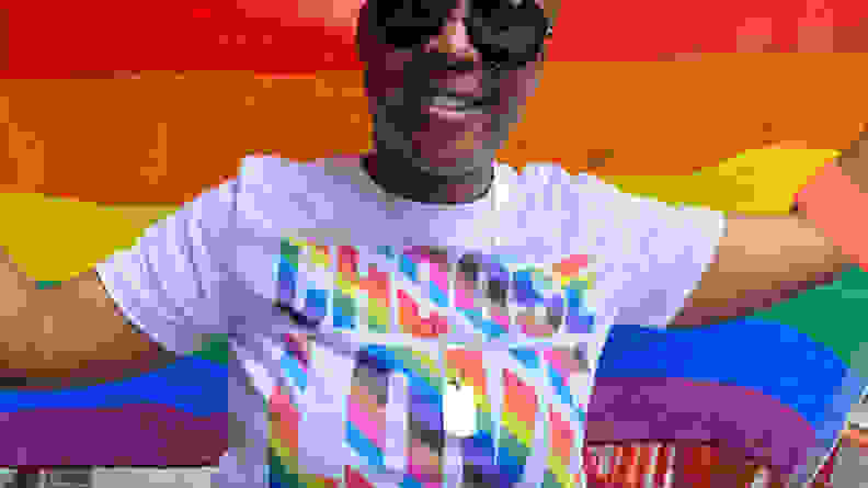 A human with a Pride flag wears a "Choose Love" shirt from the store Choose Love.