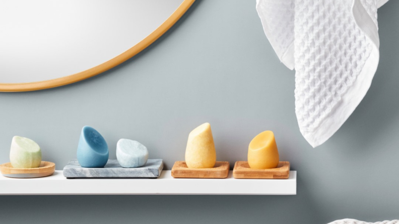 Five HiBar solid shampoo and conditioner bars sitting in dishes on a bathroom shelf.