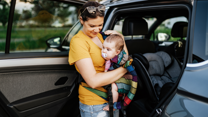 Person holding baby next to car seat.