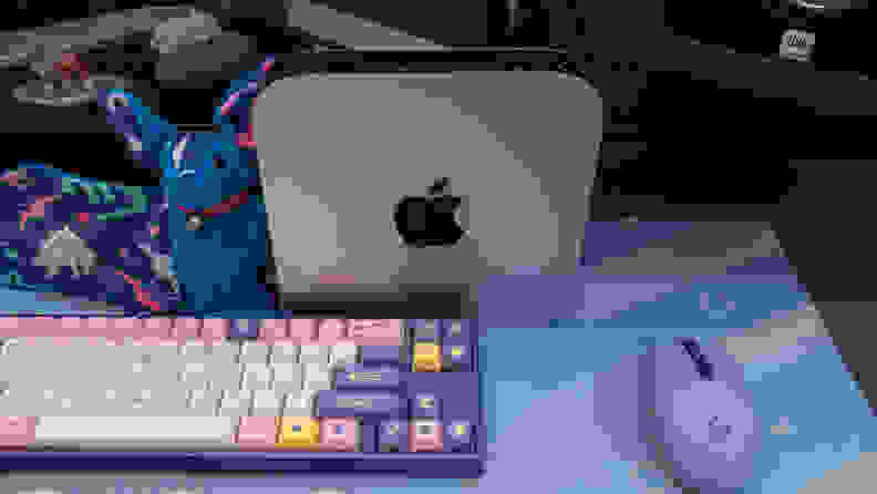 Apple Mac Mini M2 next to colorful keyboard, purple computer mouse, and plush stuffed animal.
