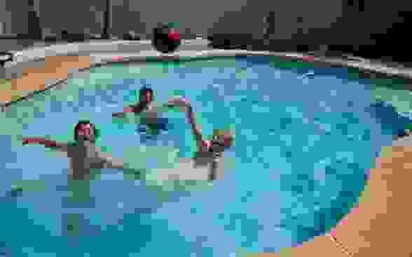 Three youths play pool basketball in an in-ground swimming pool.