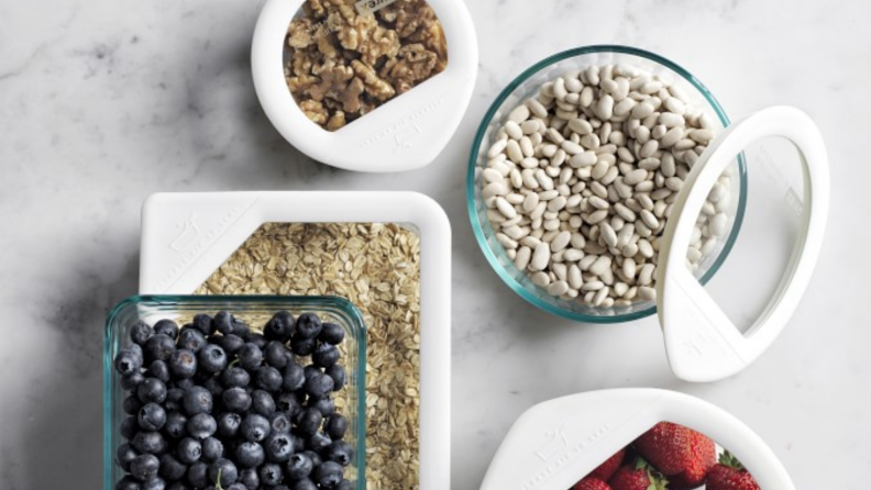 An image of Pyrex storage containers with various fruits and beans stored inside, as seen from overhead.