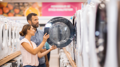 A young woman and man hold open a washing machine door in a department store