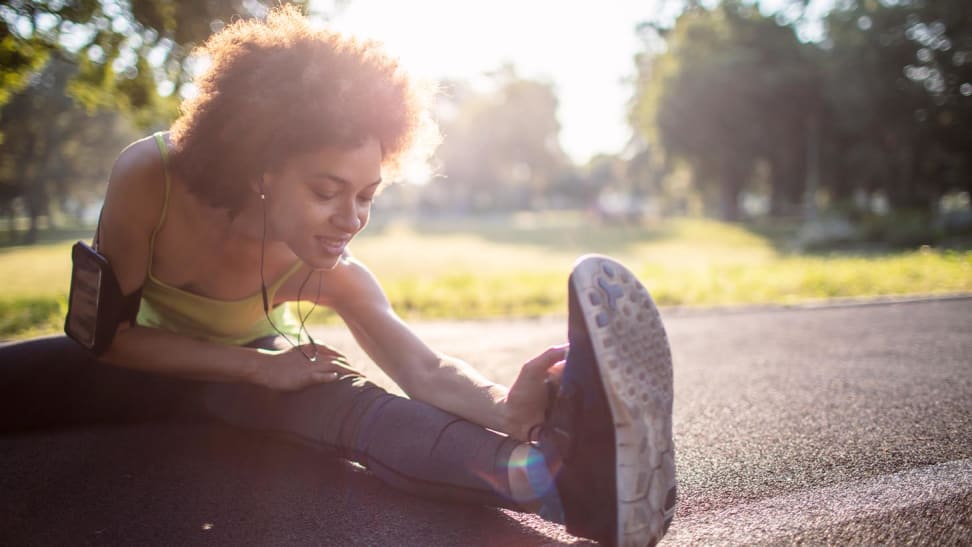 A woman wearing workout gear stretching on pavement outside.