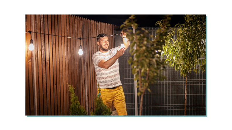 A person setting up some patio lights while they're turned on.