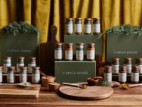 Four Spice House boxes and dozens of spice jars laid out on a wooden countertop.