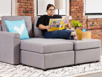 A person reading a book on a modular couch in front of brick wall indoors with their feet crossed at the ankle.
