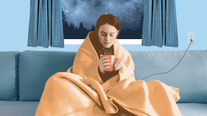 woman sitting on the couch in front of the window drinking tea wrapped in electric blanket