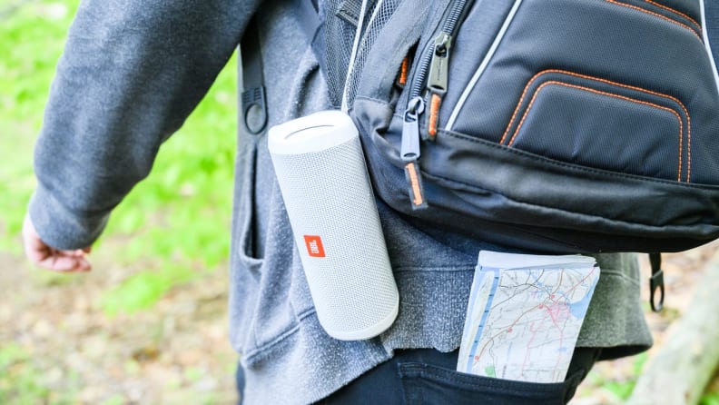 A person hikes with a speaker clipped to their backpack.