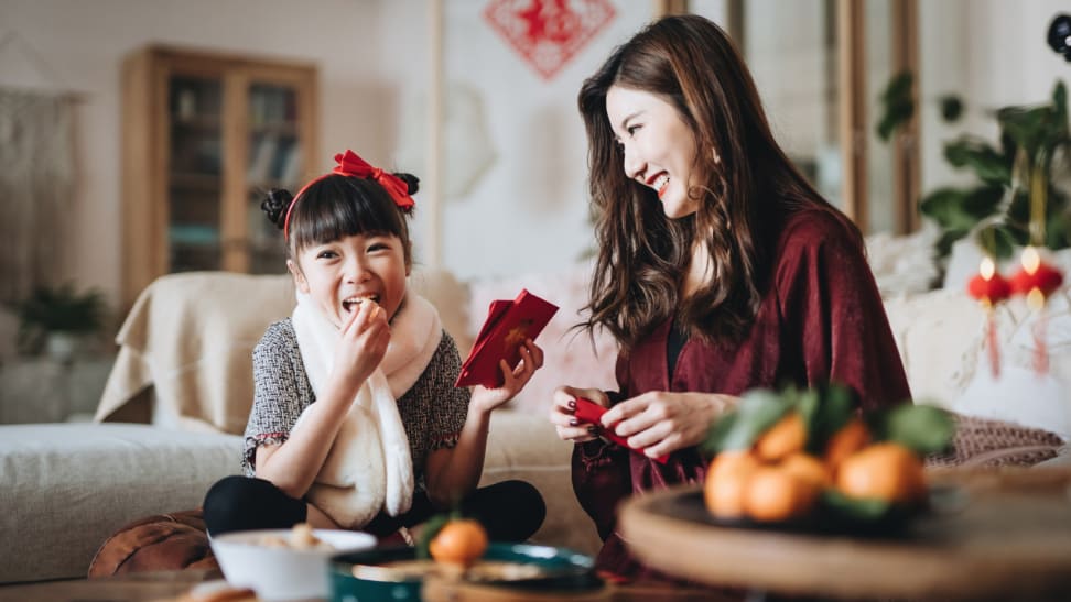 Young girl eating snacks while her mother prepares red envelopes for Lunar New Year