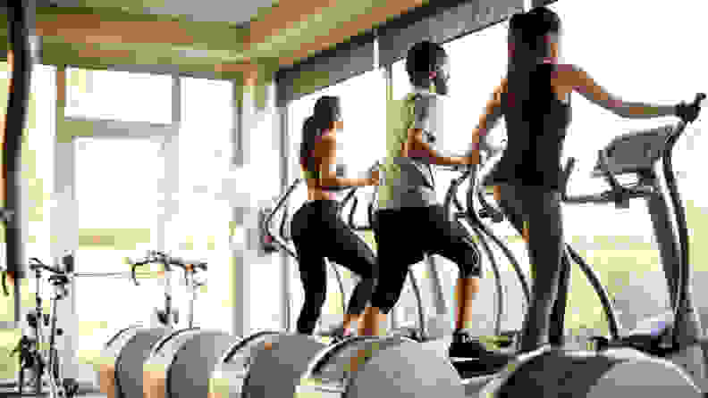 Three people using elliptical machines at the gym.