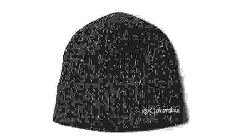 Displayed against a white backdrop, a knit black Columbia hat has bits of white in it, creating an ashy pattern like television static.