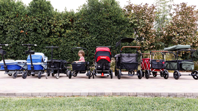 A row of strollers with a young child sitting in one and smiling at the camera.
