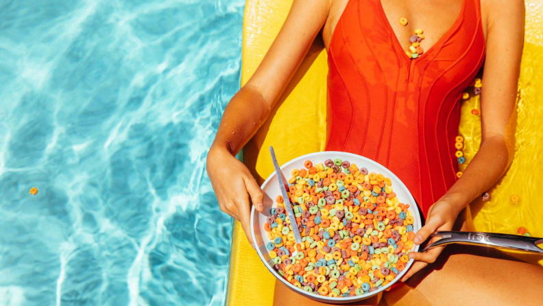 A bathing suit-wearing person, who's sitting on a yellow float in a pool, is holding and potentially eating cereal from a Frök frying pan.