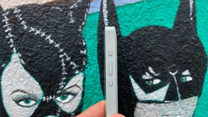 Person holding a small smartphone in front of a painted wall.
