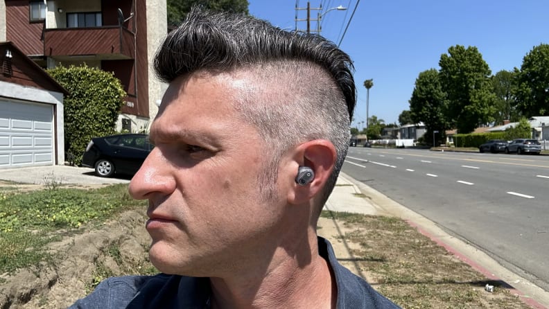 A man in a blue collared shirt wearing the Beats Studio Buds Plus out on a street.