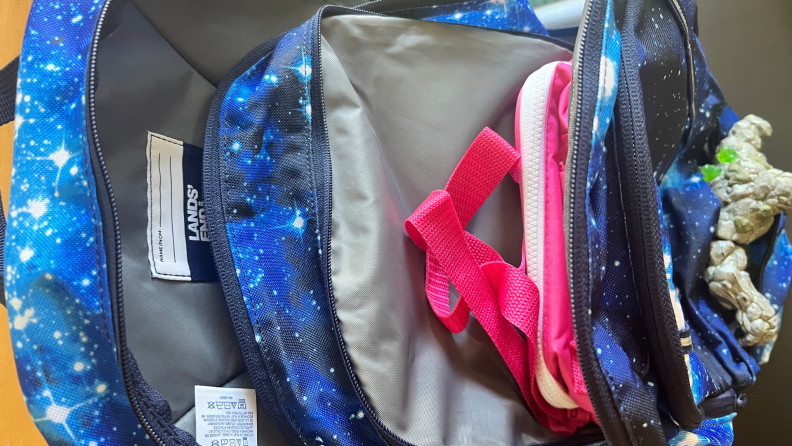 Horizontal view of the Lands' End ClassMate XL backpack's compartments with lunchbox and action figure inside.