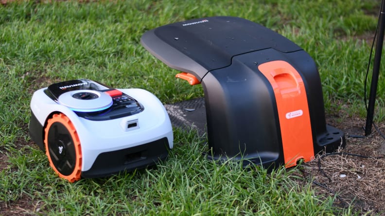 The Segway Navimow robot lawn mower sits in the grass next to it's base station