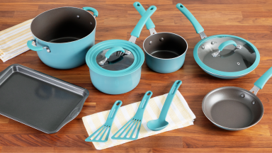 Turquoise blue colored pans, pots, lids and cooking utensils next to small rectangular baking sheet on top of wooden countertop surface.